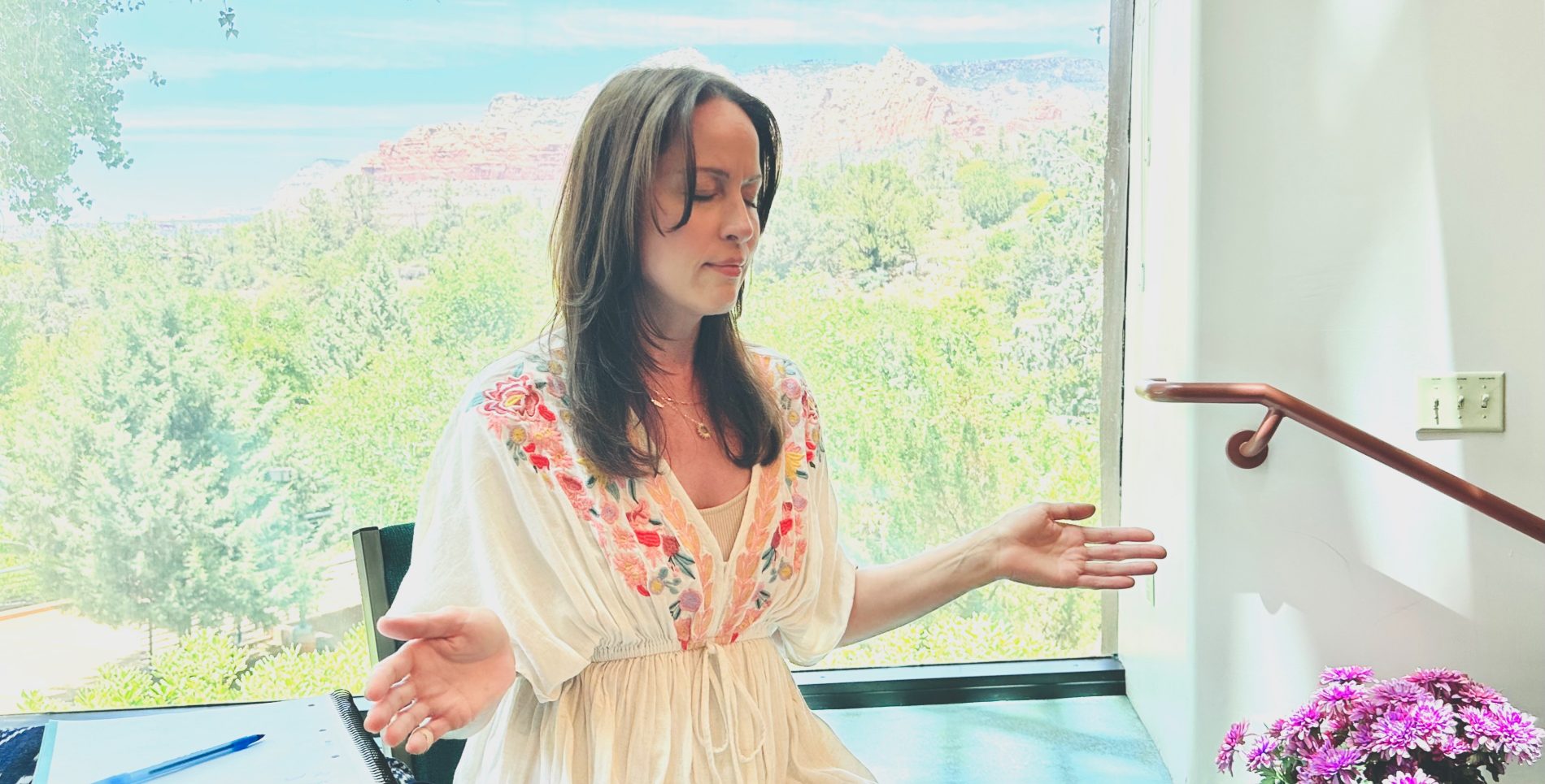 Alyssa Malehorn teaching in Sedona, hands open, red rocks beyond the window
